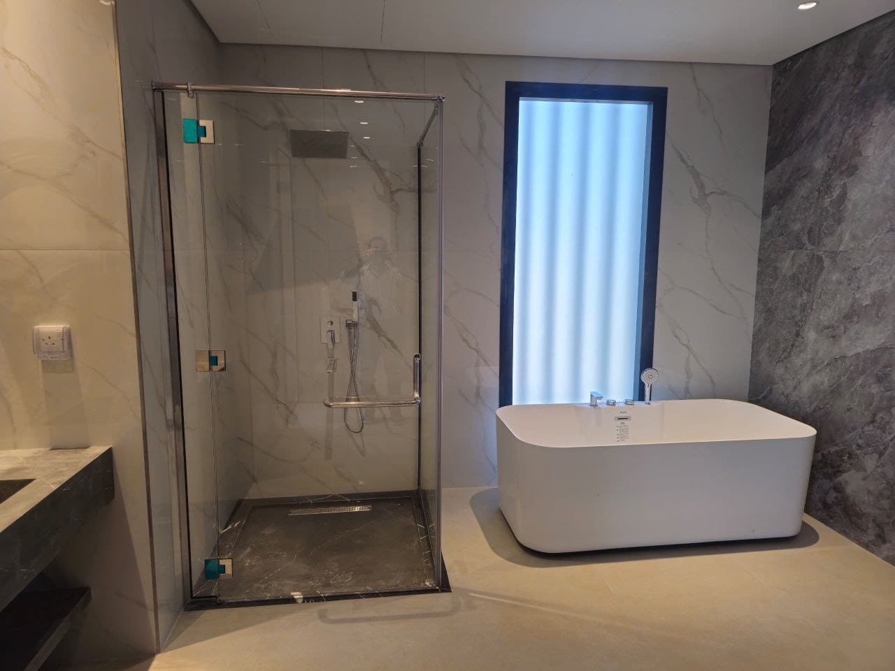 Hinged glass shower enclosure in a marble bathroom with a freestanding tub