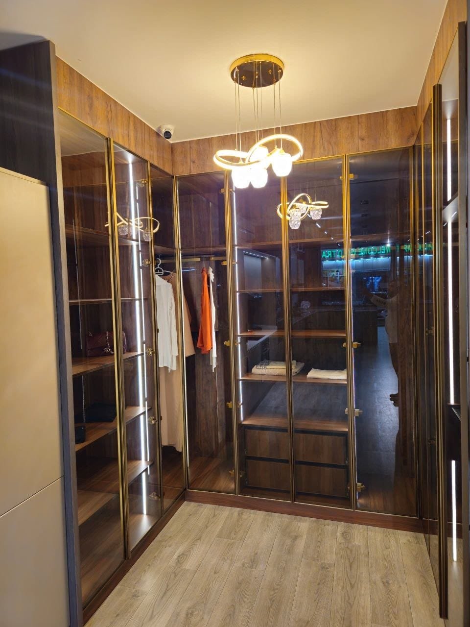 Luxury walk-in closet with bronze glass doors, gold frames and hidden lighting